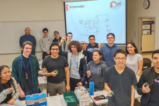 EE 110 students along with soldering mentors against the white board, from left to right: Joseph Haun, David Story and Adam Ortega