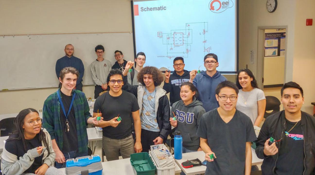 EE 110 students along with soldering mentors against the white board, from left to right: Joseph Haun, David Story and Adam Ortega